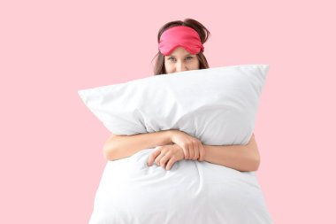 Pembe arka planda uyku maskesi ve yastığı olan genç bir kadın.