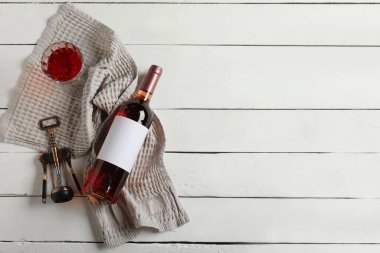 Beyaz ahşap zemin üzerinde boş etiketli, cam, açacağı ve mantarlı bir şişe şarap.