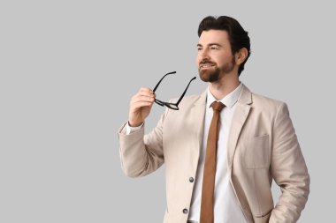 Açık arkaplanda gözlüklü, şık bej takım elbiseli yakışıklı bir iş adamı.