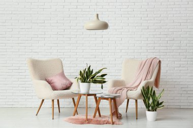 Beyaz tuğla duvarın yanında koltukları, masaları ve sansevieria bitkileriyle dolu bir oda.