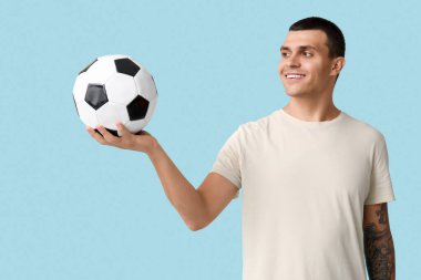 Mavi arka planda futbol topu olan yakışıklı genç adam.