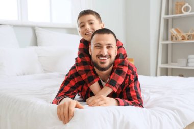 Mutlu baba ve oğlu evde yatakta damalı pijamalarıyla sarılıyorlar.