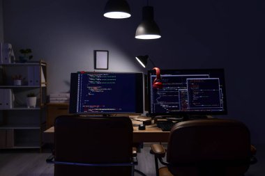 Geceleri karanlık ofiste bilgisayar monitörleri ve parlayan lambalar olan programcı masası