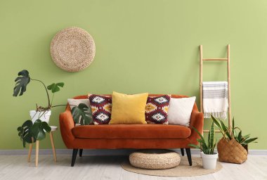 Rahat kahverengi kanepe, merdiven ve yeşil duvarın yanındaki ev bitkileri oturma odasının içinde.