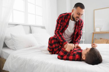 Kareli pijamalı mutlu bir baba oğluyla evde yatakta eğleniyor.
