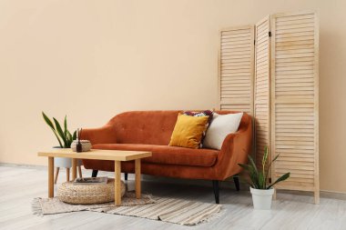 Konforlu kahverengi kanepe, masa ve katlanan ekran oturma odasının iç tarafındaki bej duvarın yanında.