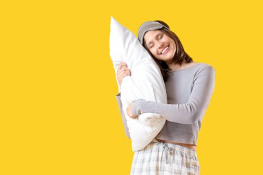 Sarı arka planda yastıklı pijamalı mutlu genç kadın.