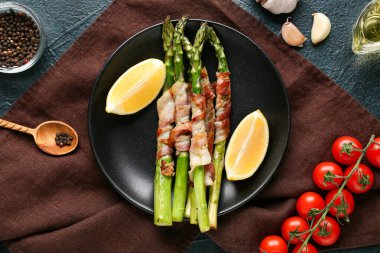 Koyu arkaplanda domuz pastırmalı ve limonlu kızarmış yeşil kuşkonmaz.