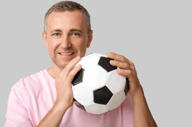 Gri arka planda futbol topu olan yakışıklı olgun bir adam.