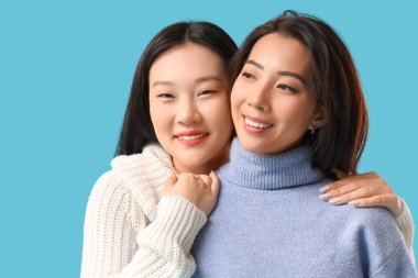 Güzel, mutlu Asyalı kız kardeşler mavi arka planda sarılıyorlar.