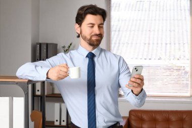 Ofiste rafların yanında cep telefonu kullanan yakışıklı bir işadamı.