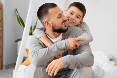 Mutlu baba ve oğlu pijamalarıyla evde yatakta sarılıyorlar.