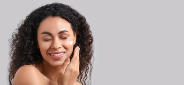 Sağlıklı cilt kremi sürmüş güzel, mutlu Afro-Amerikalı bir kadın. Gri arka plan ve metin için yer var.