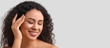 Gri arka planda sağlıklı cilde sahip güzel, mutlu, Afro-Amerikalı bir kadın.