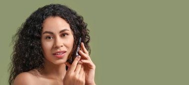 Sağlıklı cildi ve yeşil arka planda bir şişe kozmetik yağı olan güzel, mutlu bir Afro-Amerikalı kadın.