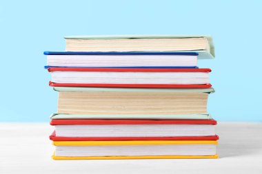 Mavi arkaplana karşı beyaz ahşap masa üzerinde renkli kitap yığını