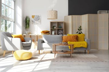 Gri kanepesi, koltuğu ve ahşap sehpası olan aydınlık oturma odasının içinde.