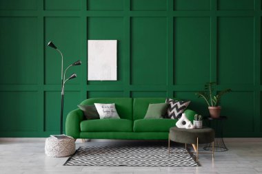 Konforlu kanepe, puf, sehpa, saksı ve yeşil duvarın yanındaki lamba.