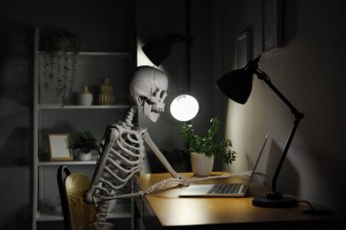 Geceleri masa başında dizüstü bilgisayarı olan insan iskelet modeli.