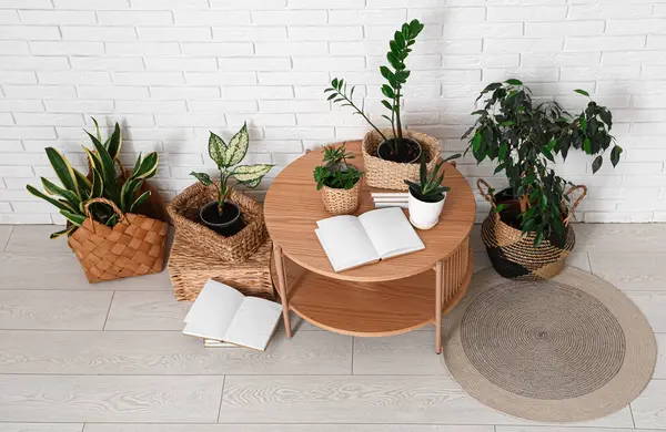 Beyaz tuğla duvarın yanında yeşil bitkilerle dolu masa ve hasır sepetler.