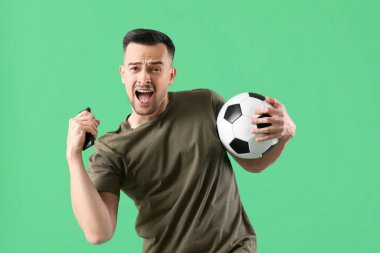 Yeşil arka planda top seyreden mutlu genç adam.