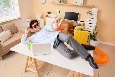 Pasaportlu genç işadamı yaz tatilini ofiste bekliyor.