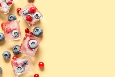 Donmuş yaban mersini ve kızılcık, turuncu arka planda buz küplerinde.