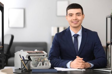 Erkek banka müdürü ofiste para sayma makinesiyle çalışıyor.