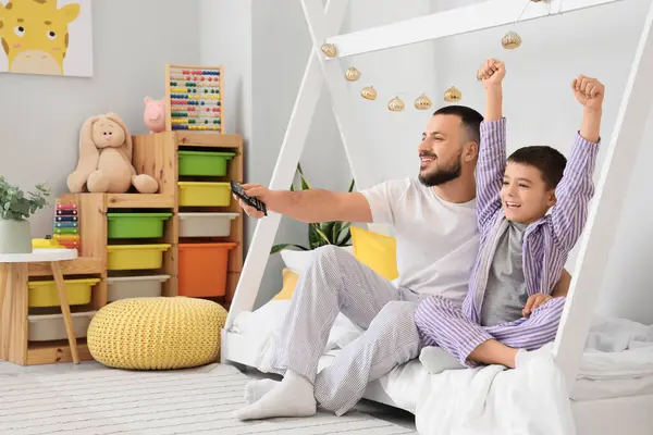 Mutlu baba ve oğlu pijamalarıyla evde televizyon izliyorlar.