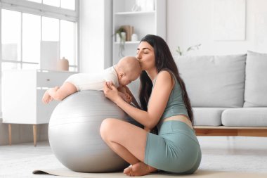 Sportif genç bir kadın evinde küçük bebeğini öpüyor.