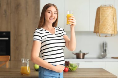 Mutfakta bir bardak meyve suyu olan hamile bir kadın.