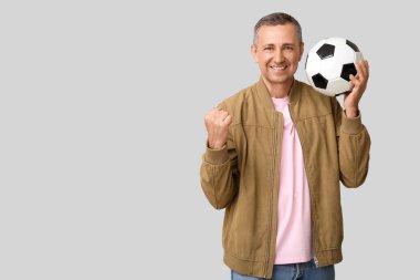Gri arka planda futbol topu olan mutlu ve olgun bir adam.