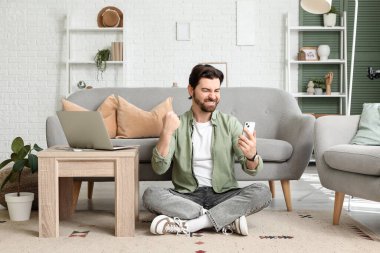 Evde cep telefonu kullanan mutlu genç adam.