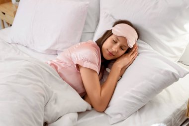 Maskeli genç bir kadın yatak odasında yastıkların üzerinde uyuyor.