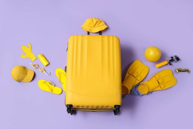 Kamera, seyahat aksesuarları ve mor arka planda bir şişe güneş kremi.