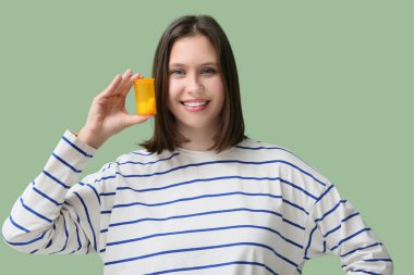 Yeşil arka planda haplarla dolu kavanozu tutan güzel genç bir kadın.