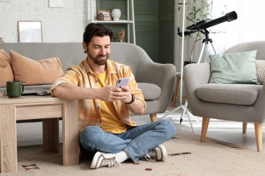 Evdeki halıda cep telefonu kullanan yakışıklı adam.