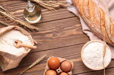 Kahverengi ahşap zemin üzerinde buğday unuyla taze ekmek, yumurta, yağ ve kağıt torbadan yapılmış çerçeve