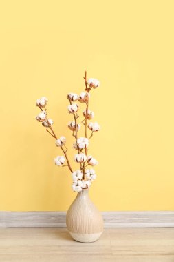 Sarı duvarın yanında yerde pamuk filizi vazosu var.