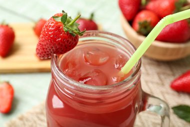 Yeşil ahşap masada çilekli mason kavanozu ve meyve suyu.