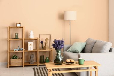 Şık oturma odasının içinde raf ünitesi, kanepe, lamba, masa ve güzel lavanta çiçekleri