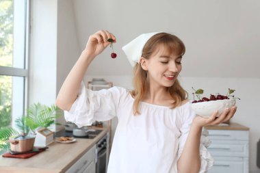 Mutfakta bir kase kirazla güzel, mutlu genç bir kadın.