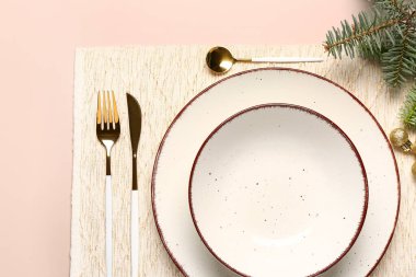 Boş tabaklar, altın çatal bıçak seti ve pembe arka planda ladin dalları ile Noel masası.