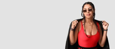 Gri arka planda rastaları olan şık, Afro-Amerikalı bir kadın.