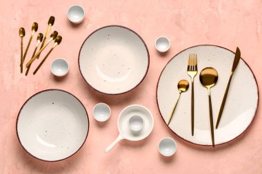 Temiz tabak, kase ve pembe masadaki altın çatal bıçak takımı.