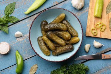 Mavi ahşap arka planda salatalık turşusu ve farklı baharatlarla dolu bir kase.