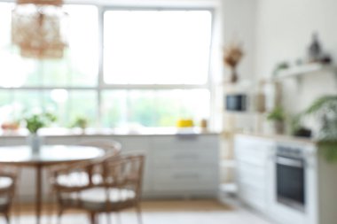 Beyaz tezgahlı, yemek masalı ve büyük pencereli aydınlık mutfağın içi bulanık görünüyor.