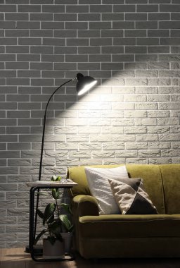 Parlayan lamba ve gri tuğla duvarın yanındaki rahat yeşil kanepe.