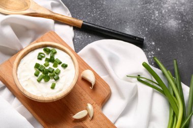 Lezzetli ekşi krema ve gri arka planda dilimlenmiş yeşil soğan tabağı.