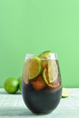 Bir bardak soğuk Küba kokteyli ve yeşil ahşap masada limon.